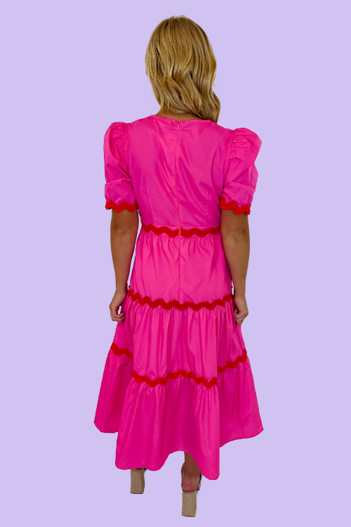 Pink in color Midi Dress Red Ric Rac on trim V-neckline Puff sleeves Tiered Bodice Zipper closure at back Lined, non-sheer 65% Polyester, 35% Cotton Model is wearing a size small
